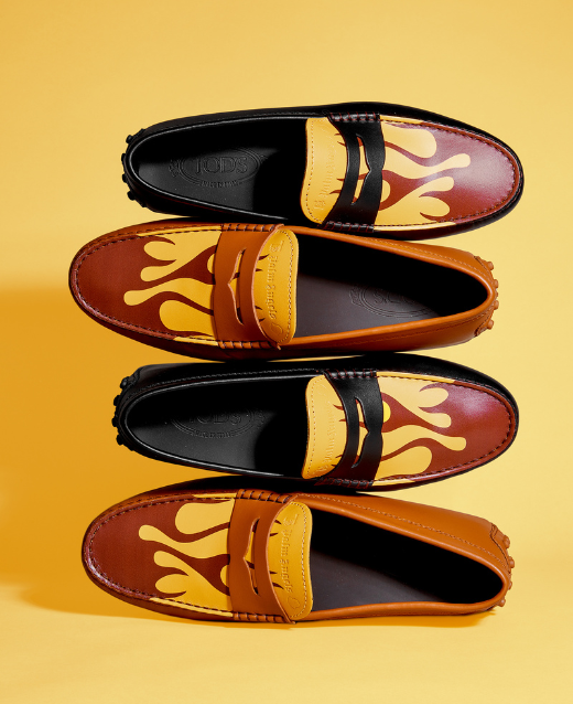 Photo of two pairs of Moncler x Palm Angels x Tod's Gommino Loafers stacked sideways on top of eachother, One pair of shoes is black, one pair of shoes is brown. Both shoes are decorated with a burgundy glame on the tongue against a yellow backdrop.