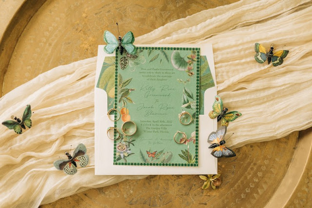 woodsy themed flatlay with green invitation and butterflies