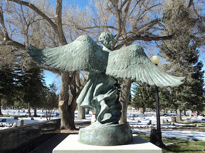 Stone statue of angel in cemetery, wings spread, seen frm behind
