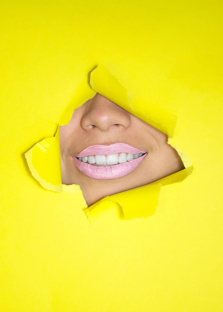 Girl smiling through yellow paper sheet; Photo by Hana Lopez on Unsplash