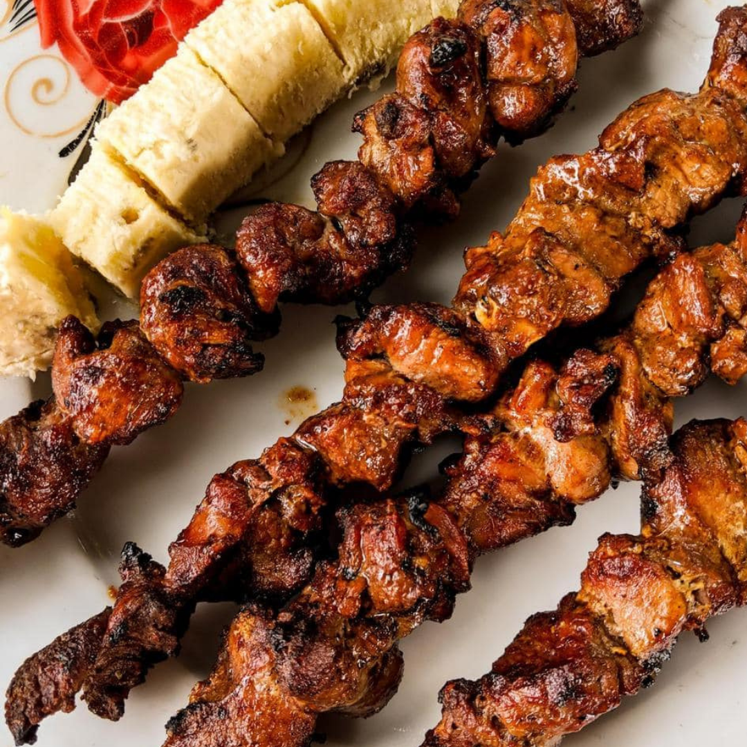 Skewers of beef brochettes sizzling on a charcoal grill at a Kigali street vendor stand.