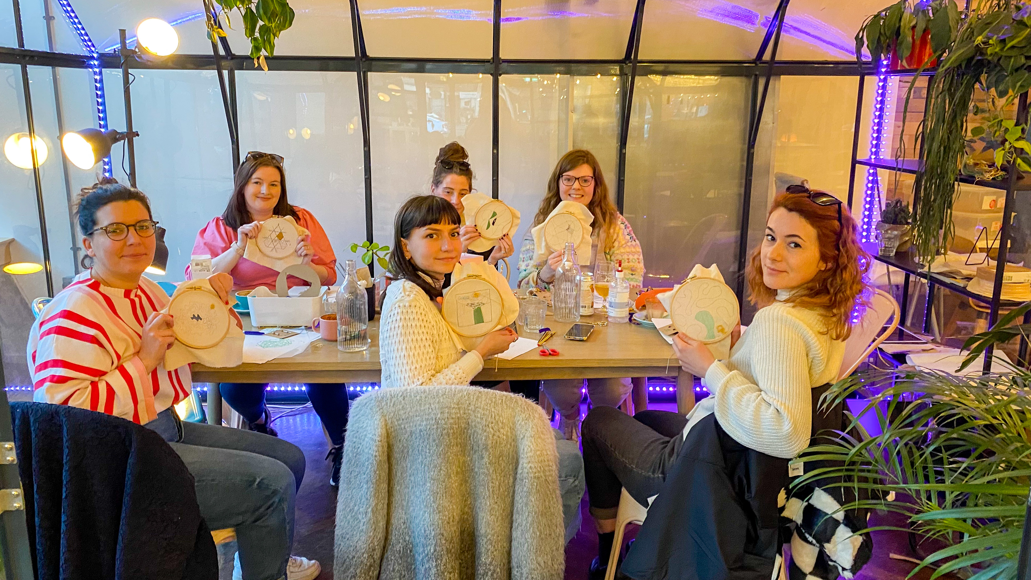 A photo of a small group of people, proudly holding their embroidery hoops to the camera. Taken at a Mindful Embroidery Workshop in Manchester ran by Stephie from Hoop & Fred.