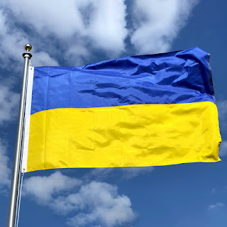 Ukraine flag on a pole in front of a light cloudy sky
