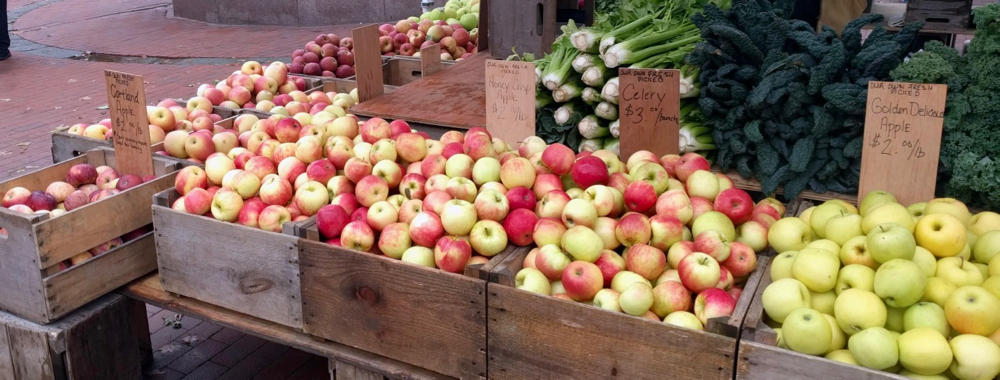 Bins filled with 6 different kinds of apples, with vegetables stacked behind them