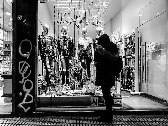 Joven de espaldas mirando un escaparate con maniquíes iluminado.