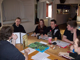 A group of players sitting around a table covered with books and dice playing a game of Dungeons and Dragons.