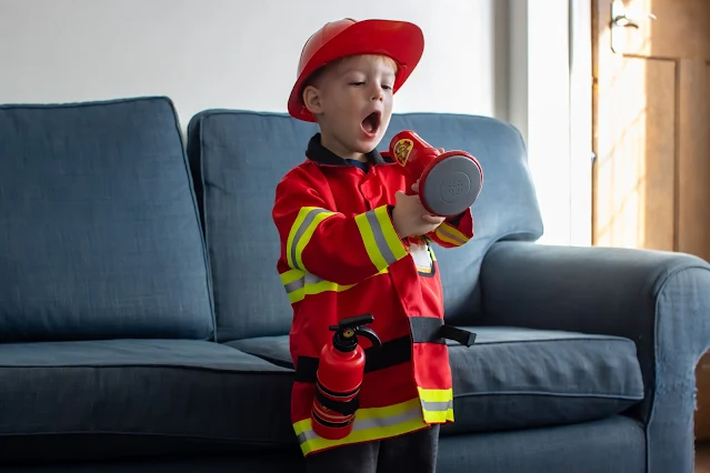 A preschool pretending to be a fireman dressed in a melissa and doug fireman costume