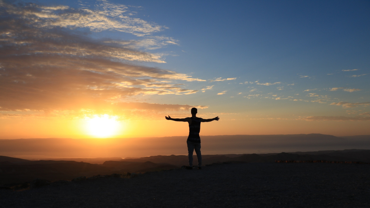 a person standing on a hill with their arms outstretched at sunset