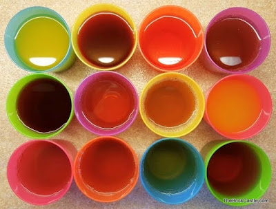 Overhead view of 12 small plastic cups filled with different coloured juice drinks