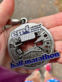 The race medal in my hand which shows and outline of Edinburgh buildings and says 'half marathon' across the bottom.