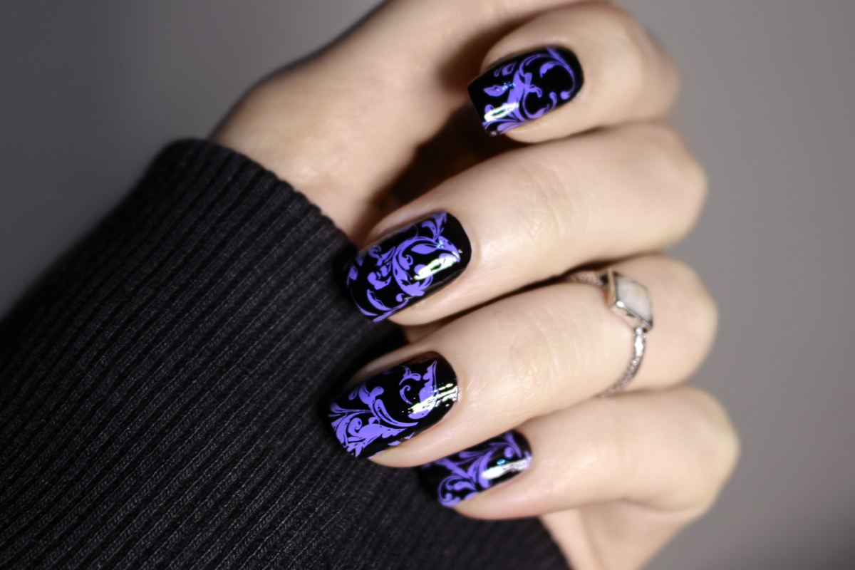 a close-up of a hand with natural long nails and goth black and purple nail look