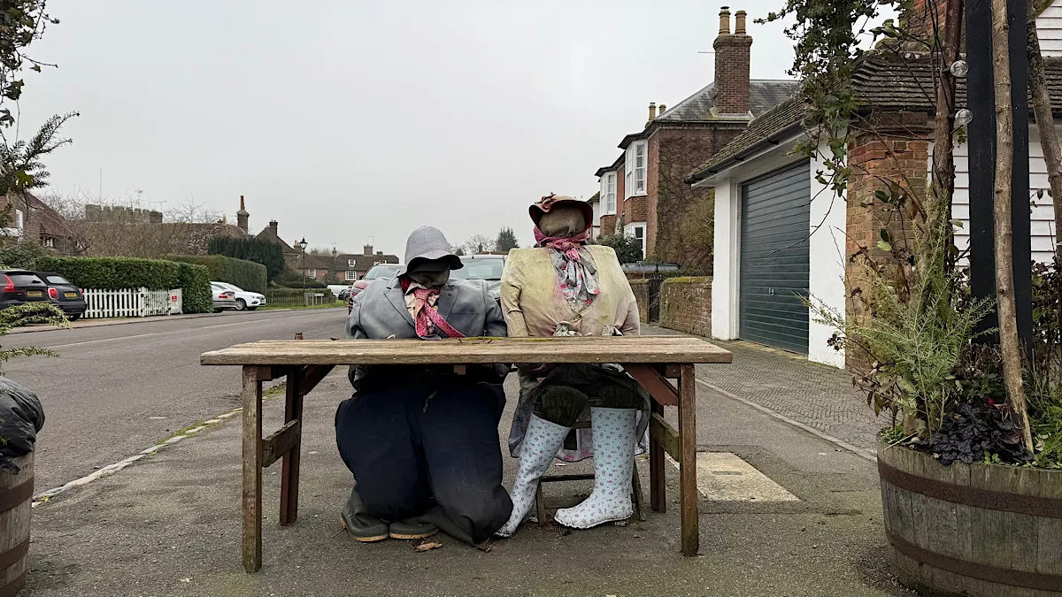 A pair of scarecrows in coats and rain hats sit at a table in Appledore, Kent