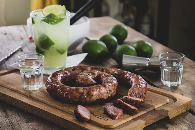 Linguiça fatiada em tábua de churrasco com caipirinha ao lado