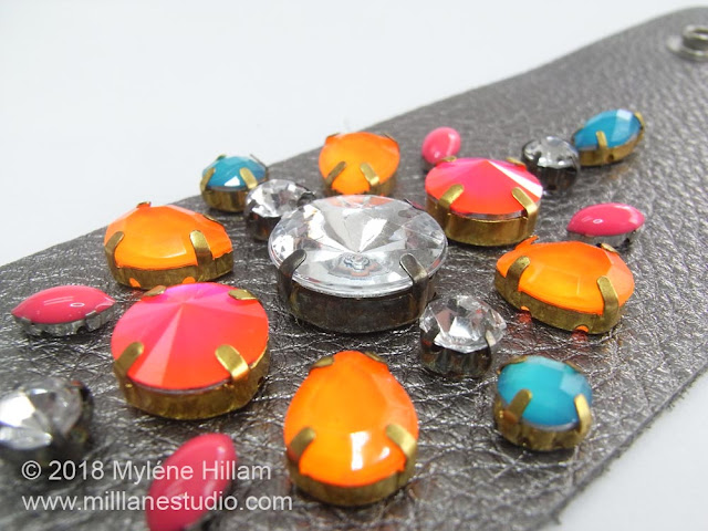 Close up of the neon bright crystals on a flat metallic leather cuff.