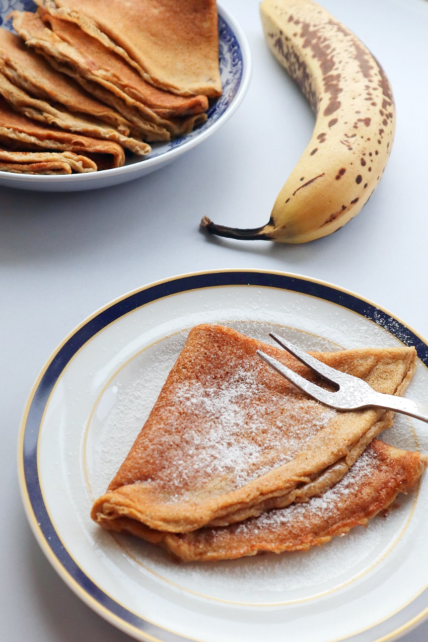 one banana crepe with powdered sugar on it served on a plate