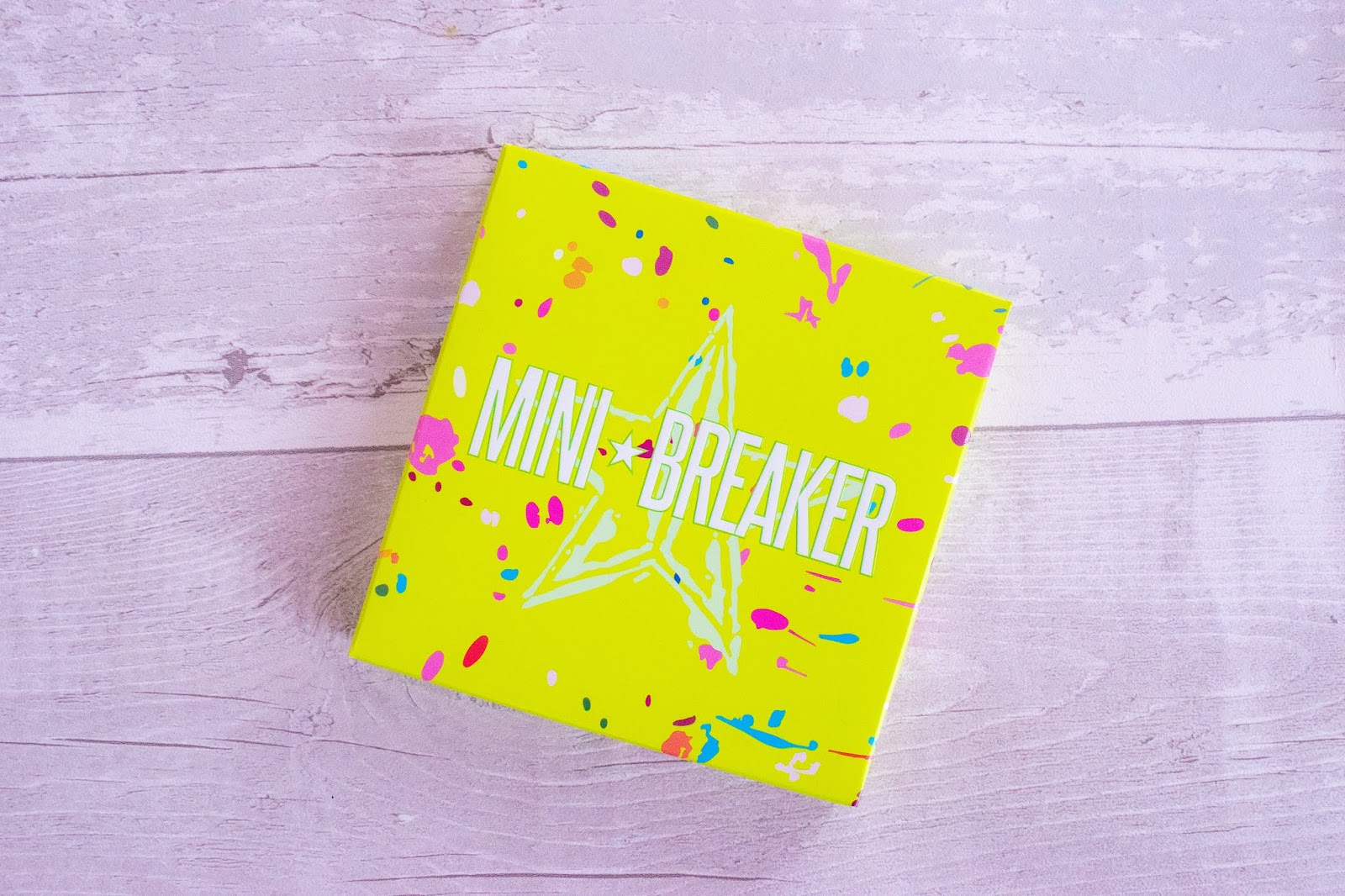 A close up of the Jeffree Star Mini Breaker Palette packaging. The box is neon green with white and pink splats over it.