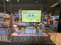 A wide set photo of a rectangular screen with a yellow background with wide white eyes a yellow sausage nose and toothy grin with bikini bottom fresh in blue cursive font with a selection of products underneath on a bright background