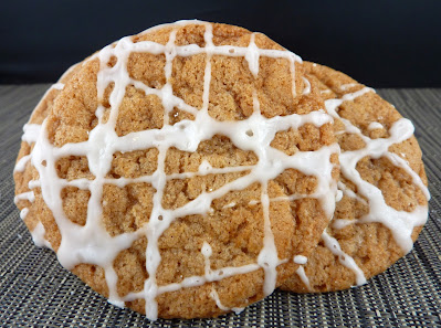 Two vegan apple cider cookies, drizzled in a criss-cross pattern with a powdered sugar glaze, photographed on a green mat
