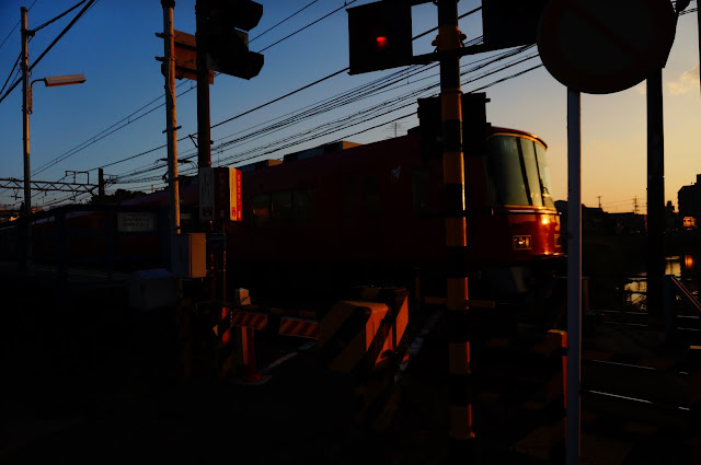 A Red train approaches as the setting sun is reflected on its windows