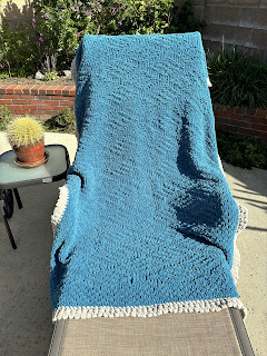 blue knitted afghan with gray trim laid over a chaise outside