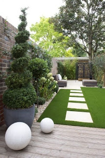 A narrow garden with white orbs and decorative trees in large urns.The seating area is to the rear past large white paving stones.