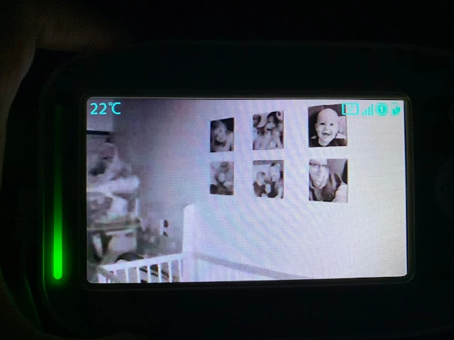 View of handheld monitor at night with camera directed towards photographs on the wall behind the cot