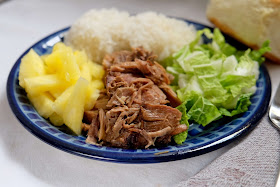 a plate of slow cooker kalua pig with fresh pineapple, hot cooked rice, sweet Hawaiian roll, and cabbage