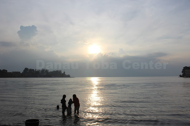 Dua orang remaja menyuci pakaian dengan latarbelakang terbenamnya matahari di lokasi pelabuhan Danau Toba Parapat