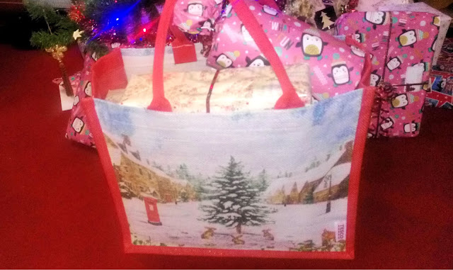 A tote bag with a snowy scene on the front, full of gifts under a Christmas tree.