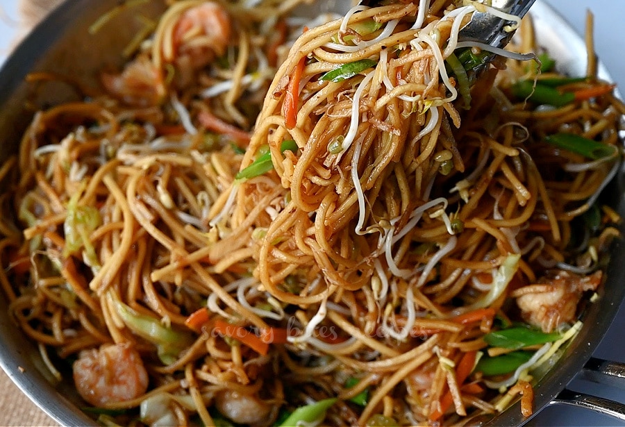 close up of a tongs holding chowmein with shrimp
