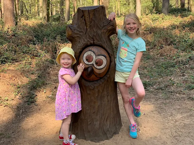 Sisters posing either side of a carving of the owl from Julia Donaldsons gruffalo at Thetford Forest