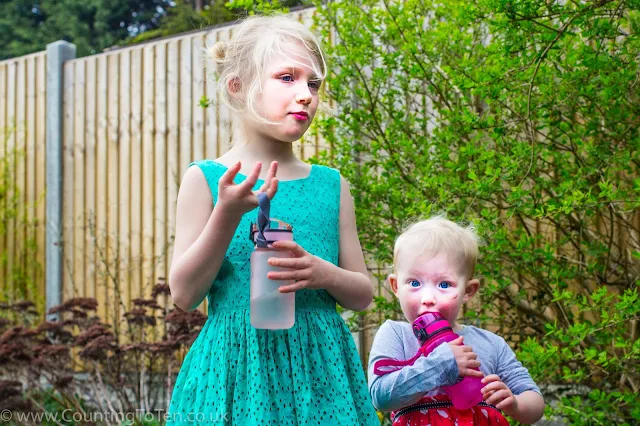 Two young girls holding water bottles, the youngest is hugging hers and kissing it