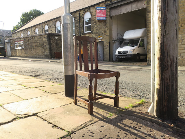 Wooden dining chair without seat beside lampost in evening light.