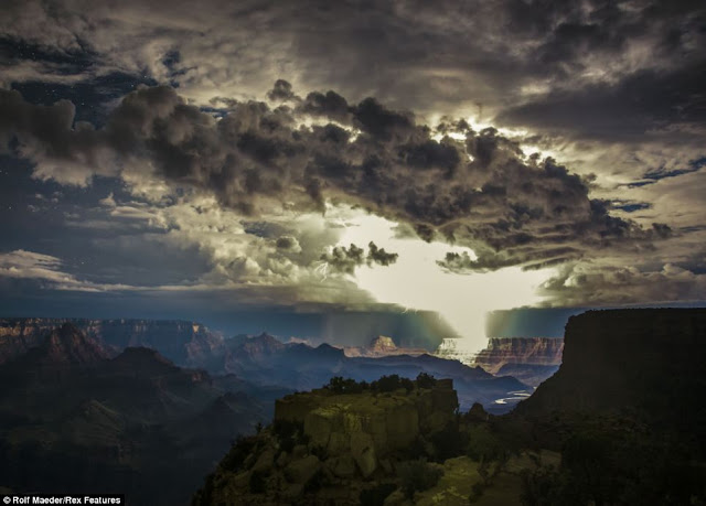 Grey clouds gather over the Grand Canyon as lightning starts to strike in the distance next to a break in the clouds