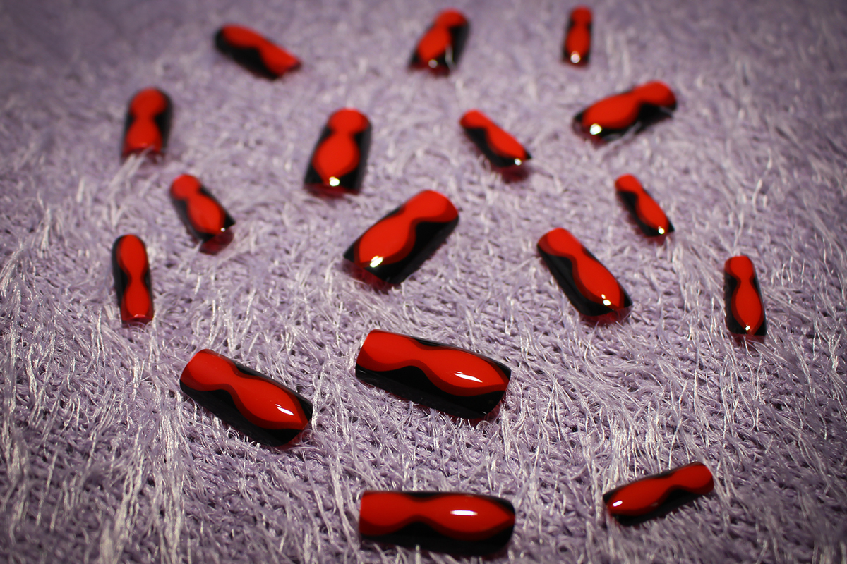 a set of red and black long press-on nails on top of a rug under the a studio's lights
