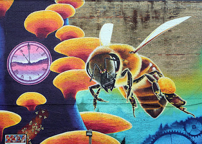 Realistic portrait of a bee, with other colourful mural elements around it including a clock face and fungi growing on a tree