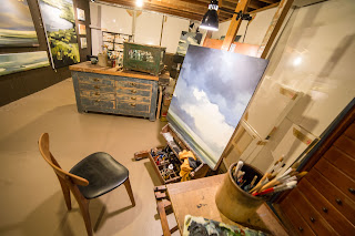A photograph of Danielle Clouse Gast's studio, showing her art on the walls and paints set up by an easel.
