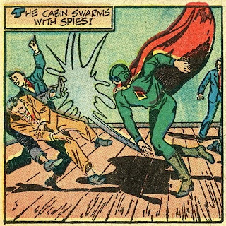 Spy Smasher! A hero in a red cape, green flight suit, aviator cap and goggles delivers a punishing blow to three men who are knocked across the room. Another man stands in the background. The logo on Spy Smasher's chest is a diamond with black center. Caption at upper left reads: "The cabin swarms with spies!"