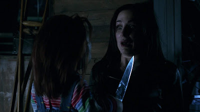 Movie still from the movie Curse of Chucky where Chucky holds a knife in Barb's (Danielle Bisutti) face