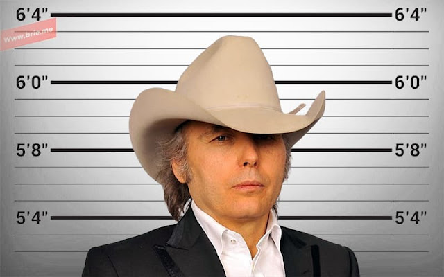 Dwight Yoakam posing in front of a height chart background