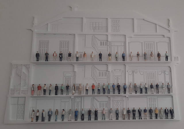 uma maquete de um perfil de um museu com bonecos pequenos de várias pessoas