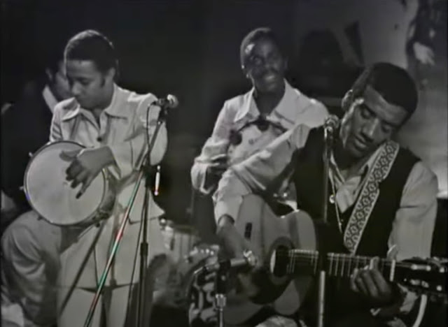 Screenshot of Jorge Ben playing his guitar and singing along with his Trio Moctoto on the Italian TV show Speciale Per Voi on June 2, 1970 (in black & white).
