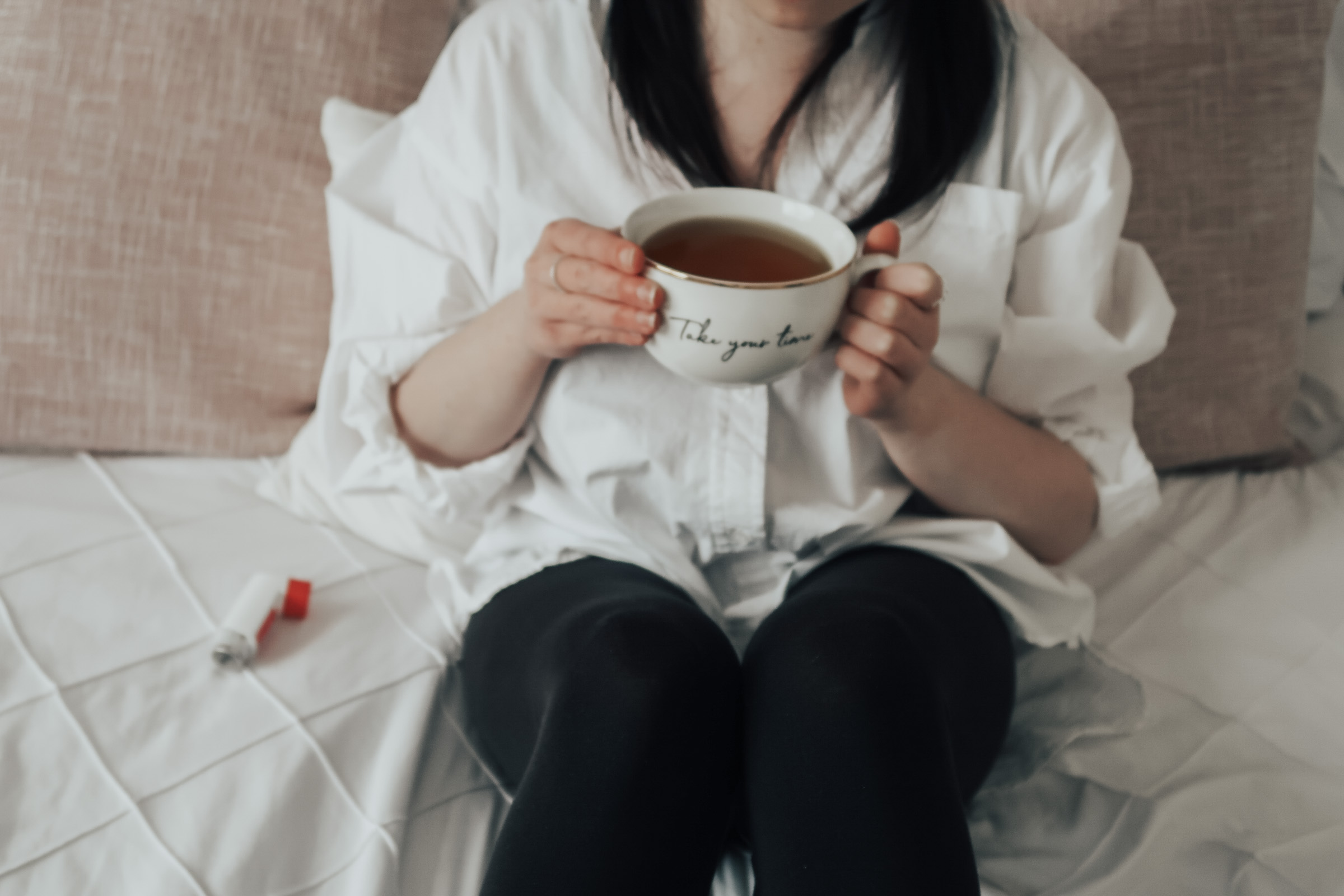 A woman sat on a bed holding a white mug.