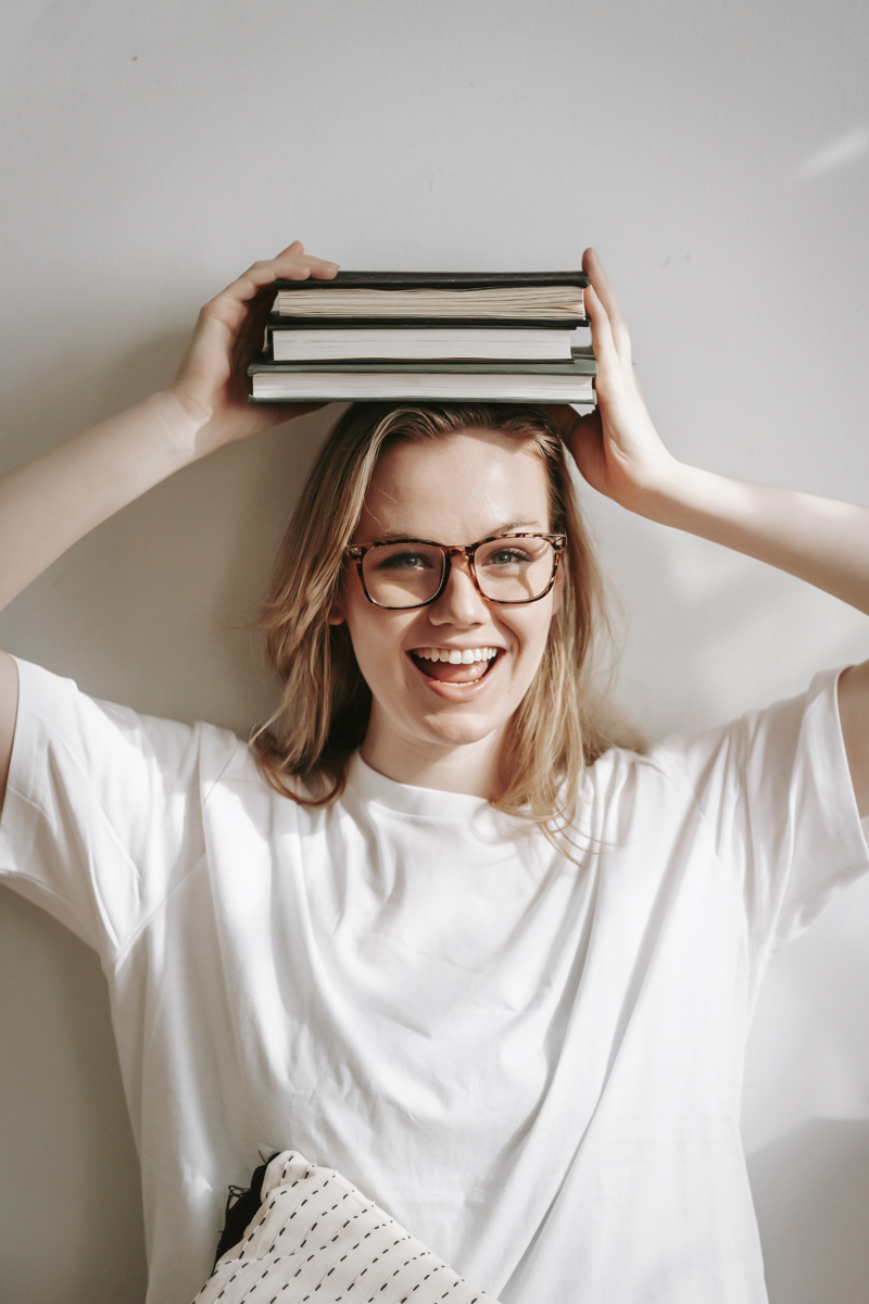 a woman in glasses is holding a stack of books on her head
