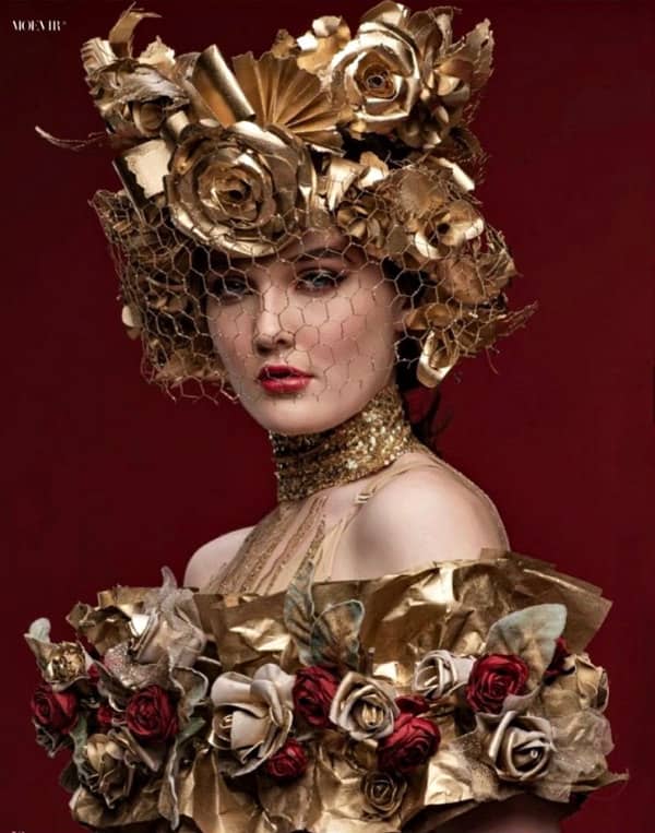 woman dressed in elaborate gold and red paper floral headpiece and top with golden see-through veil over face