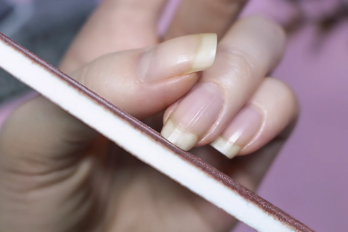 a close-up of woman's nails showing a process of filling down the nails