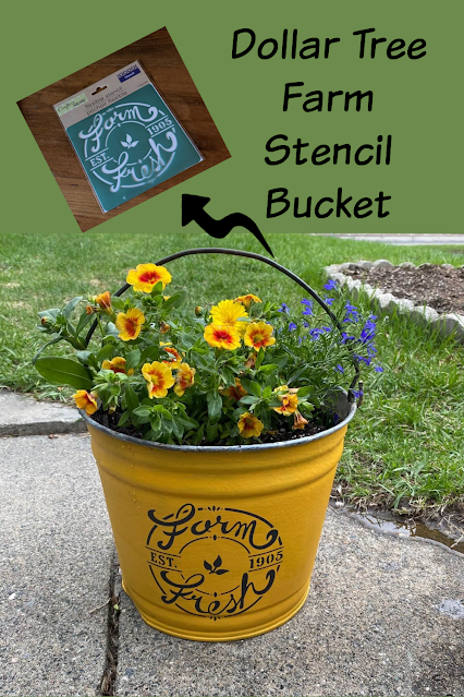 Photo of a mustard painted galvanized bucket planters stenciled with a Farmhouse Dollar Tree stencil.