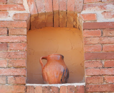 fachada de ladrillo rojo con ornacina ocre en la que hay colocado un puchero de barro