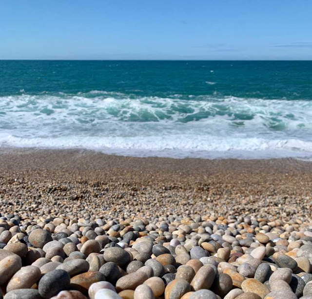 a view over a pebble beach towards the sea with waves breaking on the shoreline