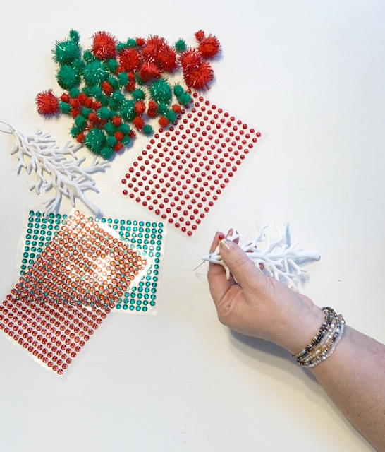 A hand holding a white tree ornament and adding red sequins to the tree branches.